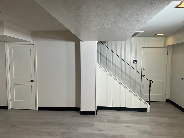 Rear view of finished basement. Left door to storage closet and right door into garage. Stairs lead into kitchen.
