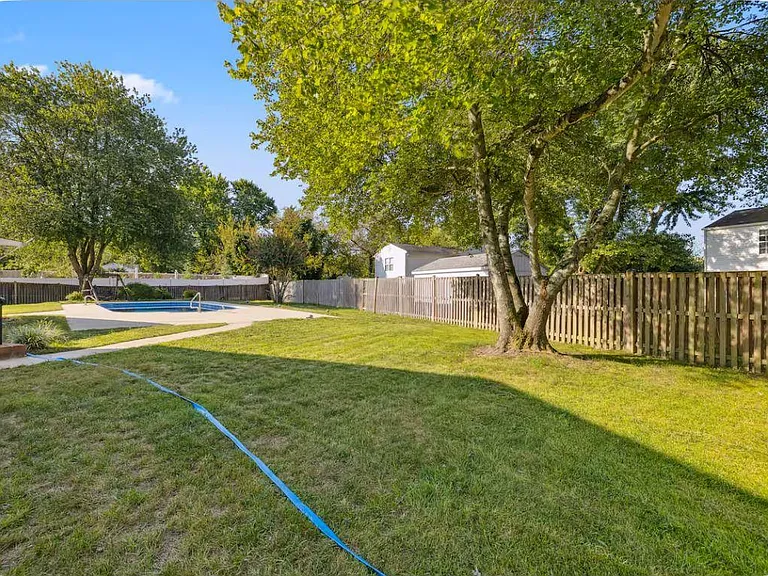 Spacious fenced backyard with mature shade trees and an in-ground pool, offering plenty of room for outdoor relaxation.