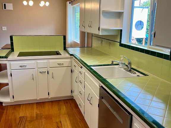 Freshly grouted tile, new dishwasher, and freshly painted cabinets with updated hardware. Electric stove with vintage 1950s vent, plus a new sink head upgrade not shown.