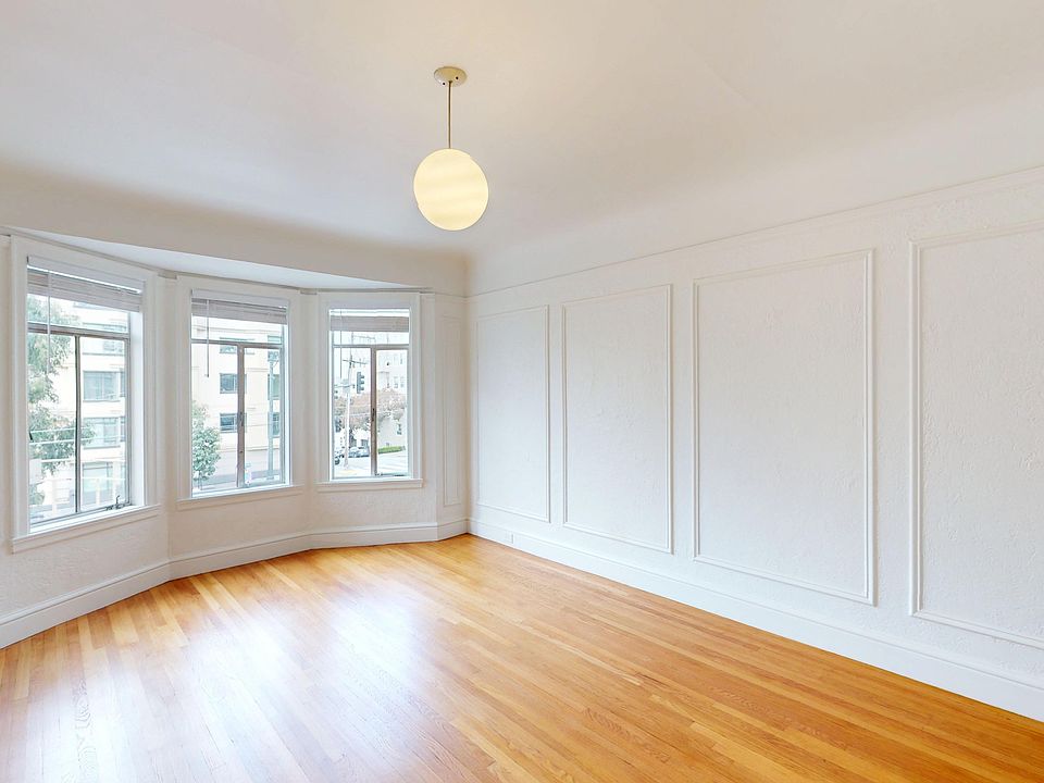 Bright room with hardwood floors and a round ceiling light, featuring large bay windows with urban views
