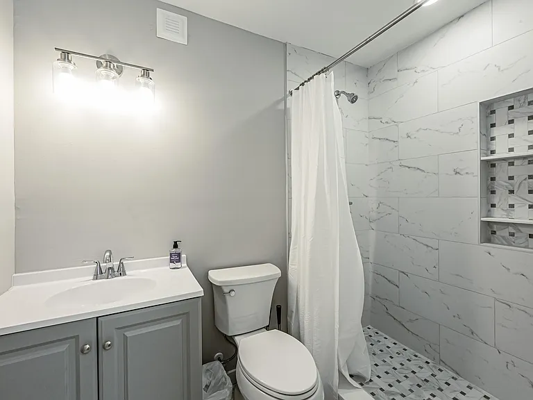 Updated bathroom with tiled tub/shower surround, built-in niche shelving, and a vanity with ample counter space.
