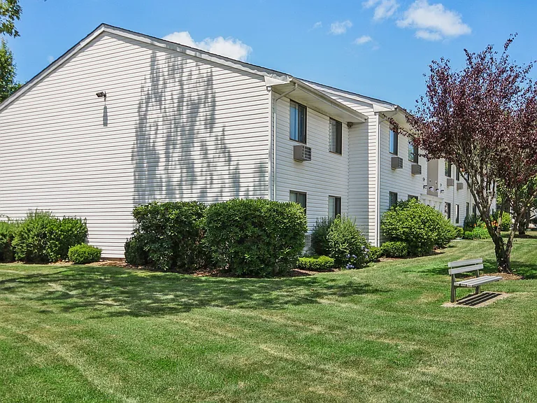 Exterior view of apartment building with green grass and bench seating