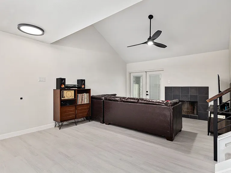 Living room with ceiling fan, french doors, high vaulted ceiling, a fireplace, and light wood-type flooring