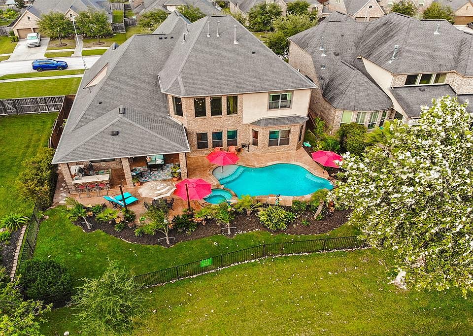 Welcome to your own piece of paradise! View of the back of the home with tropical landscaping, outdoor kitchen, iron fence with lights and view that looks directly onto the area lake.
