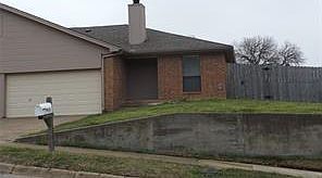 View of front facade featuring a chimney, brick siding, fence, concrete driveway, and an attached garage