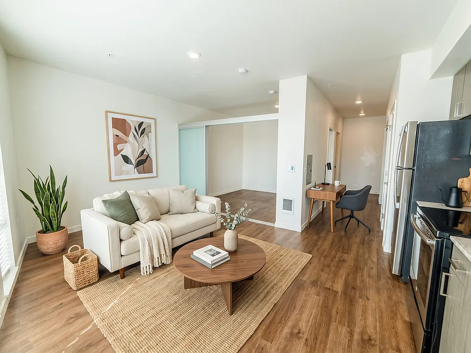 Bright open-concept living space at Vibe Apartments in Seattle featuring wood-style floors, a dedicated study nook, and sliding doors into the bedroom.