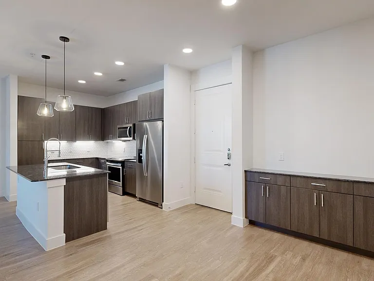 Apartment kitchen with stainless steel appliances, dining and living room with wood-style flooring.