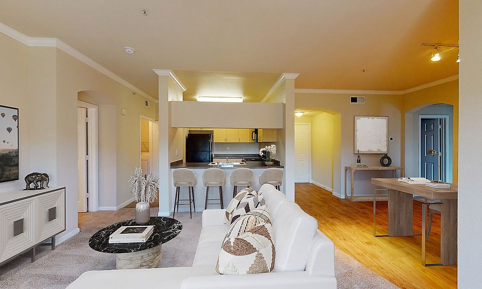 Carpeted and staged living room with work-from-home setup and kitchen.