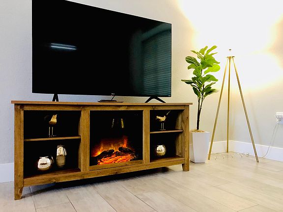 The living room features a large flat screen smart TV. The TV stand has a fire feature with an optional heater.