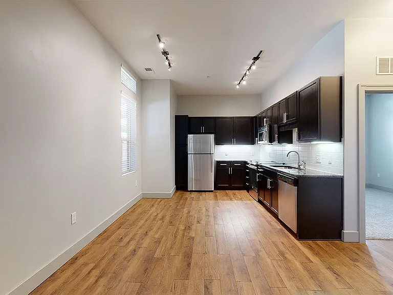Apartment kitchen with stainless steel appliances, dining and living room with wood-style flooring.