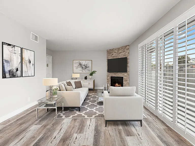 Hardwood floored living room with stone accented fireplace and large exterior windows.
