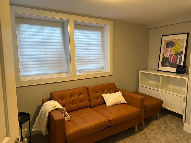 The cozy living area features extra closet storage, a media console with a large Smart TV, and a comfortable loveseat with an ottoman for ultimate relaxation.
