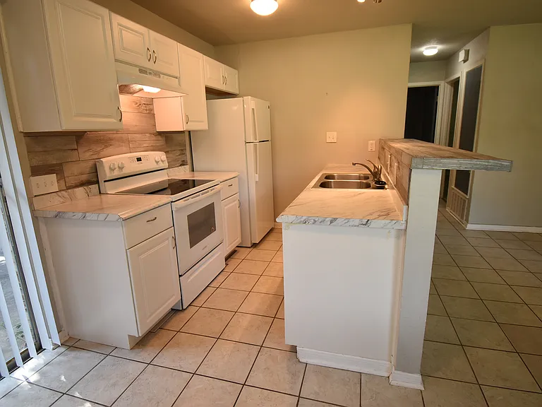 This view of the kitchen clearly shows the walk-up bar, new refrigerator and very clean electric stove.