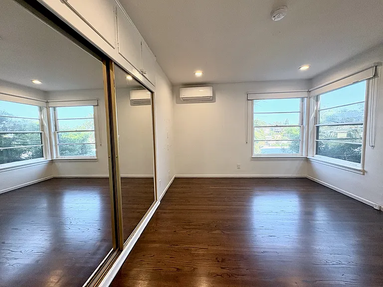 Master bedroom with generous mirrored built-in wardrobes, large windows, and leafy views.