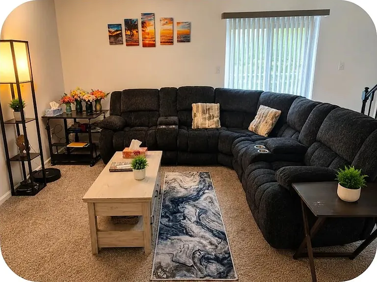 Spacious living room with a large sectional, coffee table, and side tables, plus window blinds for controlled natural light.