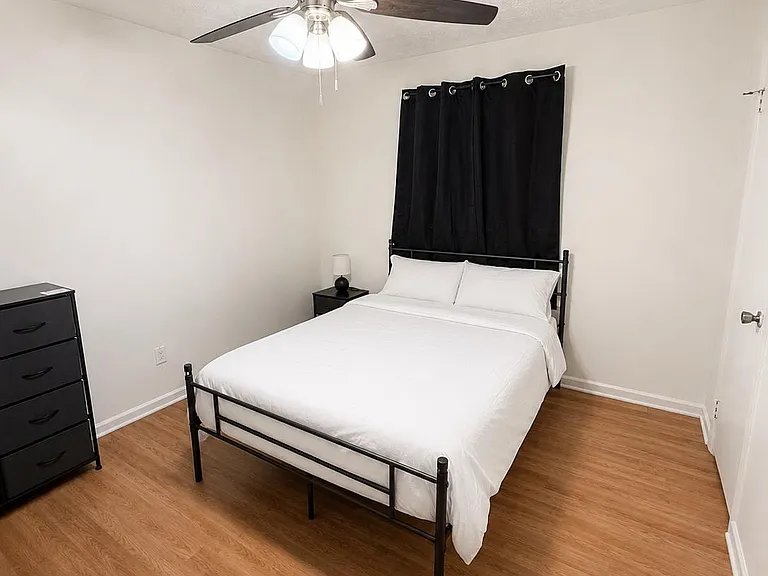 Furnished bedroom with wood-look flooring, ceiling fan with light, and space for a dresser and nightstand.