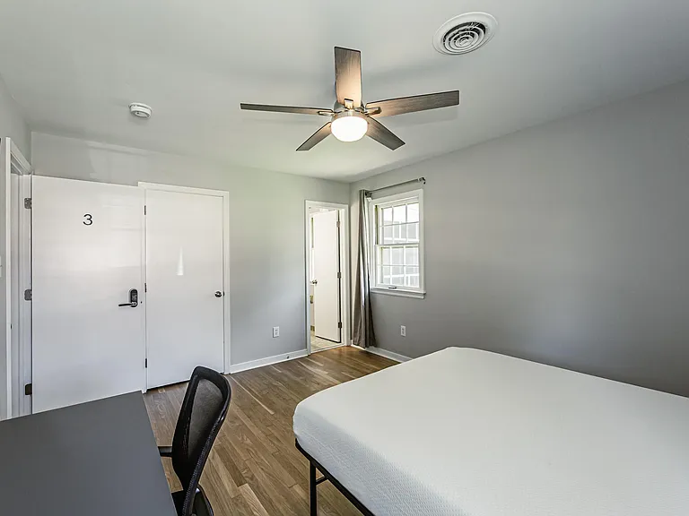 Private bedroom with hardwood floors, ceiling fan, and a window with curtains, plus a keyed entry and space for a desk.