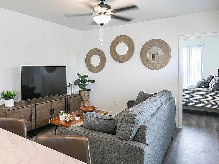 Chic and cozy living room with modern gray sofa, elegant wall decor, and large TV, leading to a bright bedroom with stylish decor.