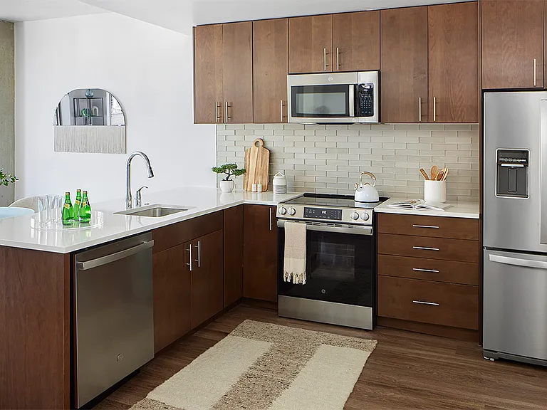 Apartment kitchen with stainless steel appliances, quartz countertops, and wood-style flooring.