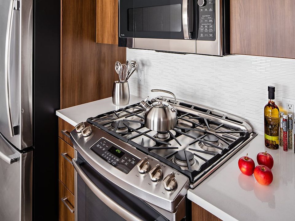 Signature Collection Kitchen with oak cabinetry, light grey quartz countertops, white tile backsplash, upgraded stainless steel appliances, and hard surface plank flooring