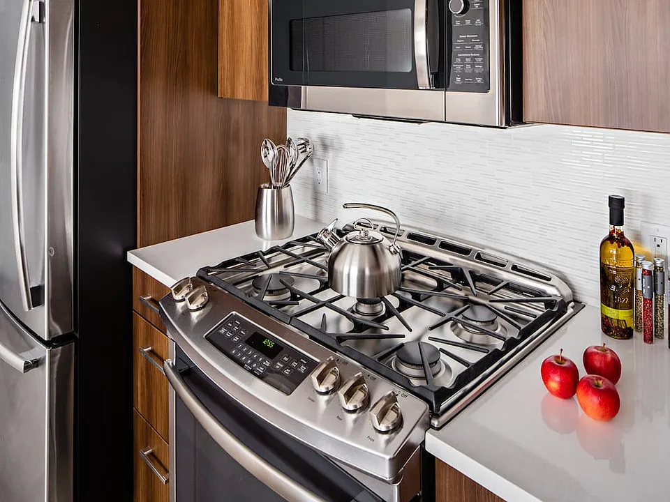 Signature Collection Kitchen with oak cabinetry, light grey quartz countertops, white tile backsplash, upgraded stainless steel appliances, and hard surface plank flooring