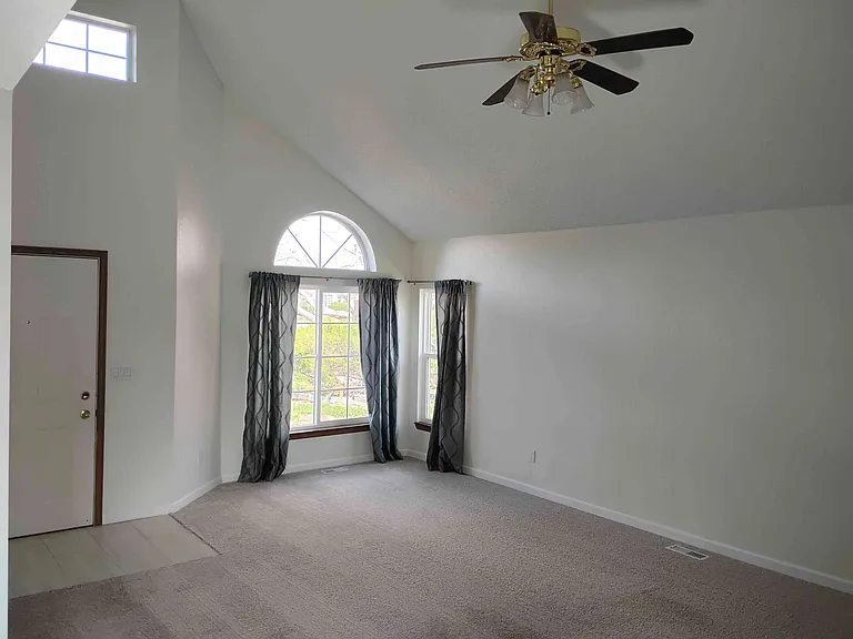 Living room has vaulted ceiling, bookshelves and a fireplace. Also has ceiling fan.