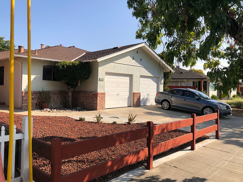 Front yard, driveway parking, kitchen window next to tree, white colored garage door shown