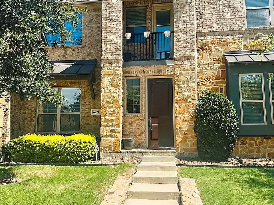 View of front facade with stone and brick siding, a front lawn, and a balcony