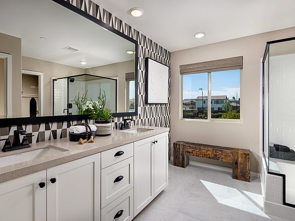 A modern and spacious bathroom with white cabinets, a large mirror, and a window overlooking an outd