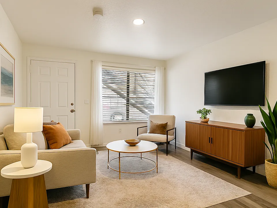Bright, modern living space with clean lines, natural light, and warm wood flooring. Features a large window with blinds and sheer curtains, recessed lighting, and a spacious layout ideal for flexible furniture arrangements and personal styling.