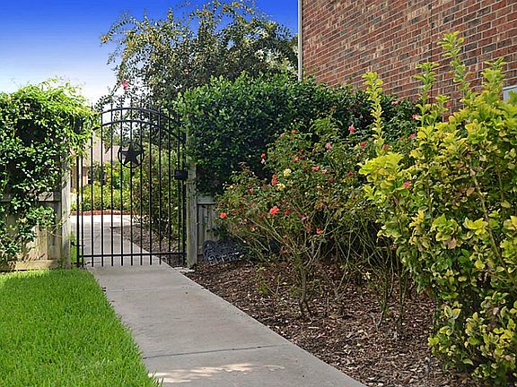 Beautiful gardens wrap around the home as witnessed here with this walkway that leads from the backyard thru this arched wrought iron gate to the driveway.