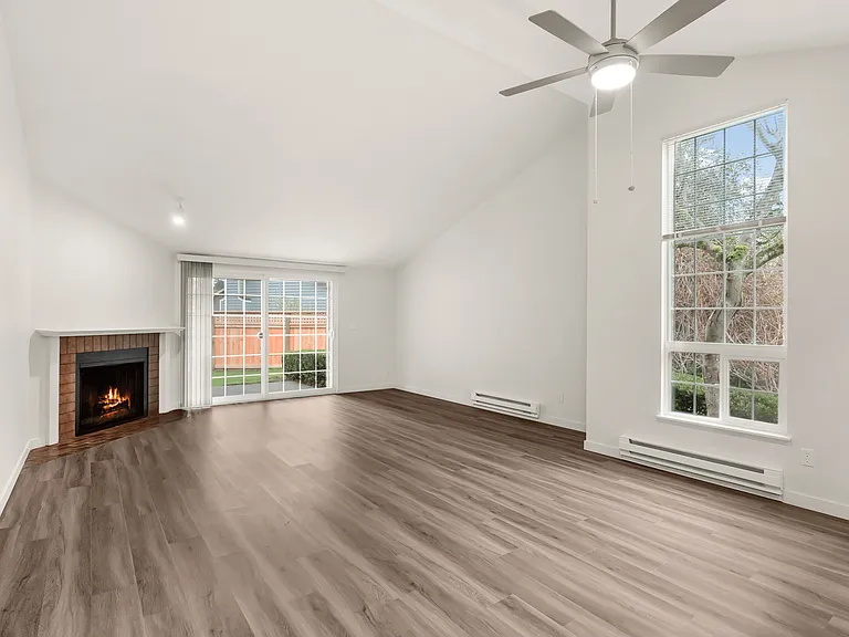 Bright and airy living room with a cozy fireplace, modern ceiling fan, and large windows overlooking a private garden. Bright and airy living room with a cozy fireplace, modern ceiling fan, and large windows overlooking a private garden.