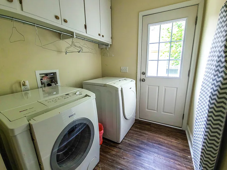 Laundry room and access to the fully enclosed yard. Laundry room has a Bosch washer and dryer, iron and ironing board, laundry drying rack, laundry soap, and bleach