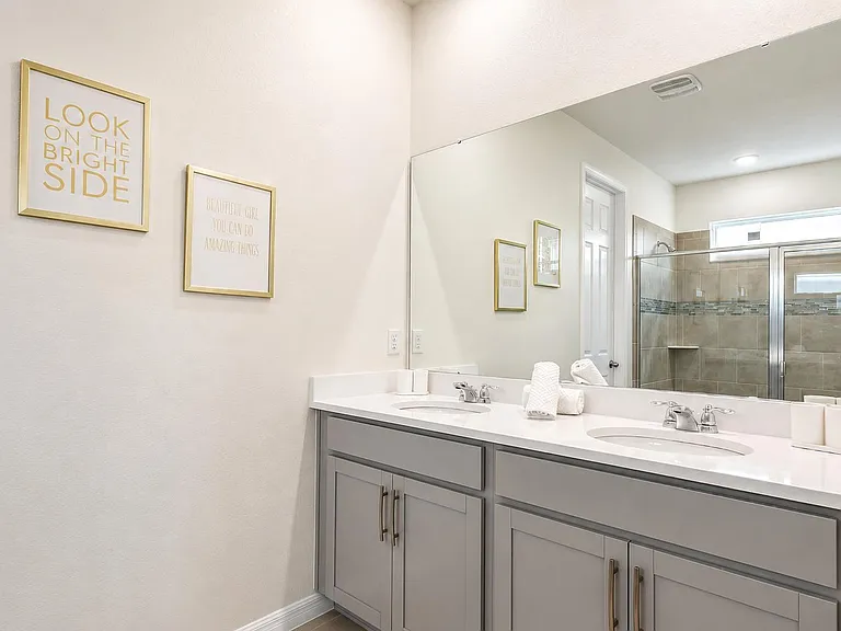 Spacious bath with a double-sink vanity, large wall mirror, and a tiled walk-in shower with glass doors.