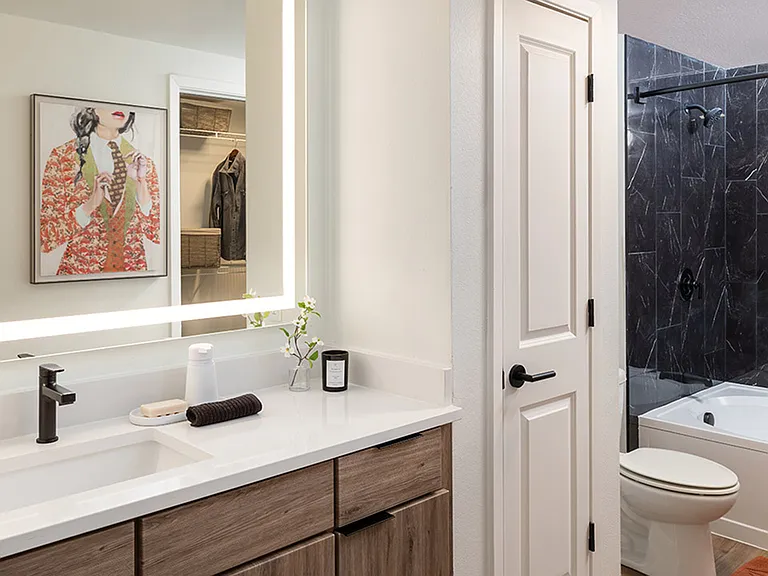 Apartment bathroom with large soaking tub, wood-style flooring and LED vanity mirror.