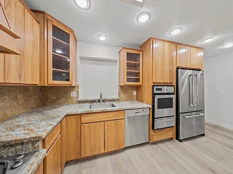 Kitchen with ample wood cabinetry, stone-look counters, tile backsplash, and stainless appliances for everyday cooking.