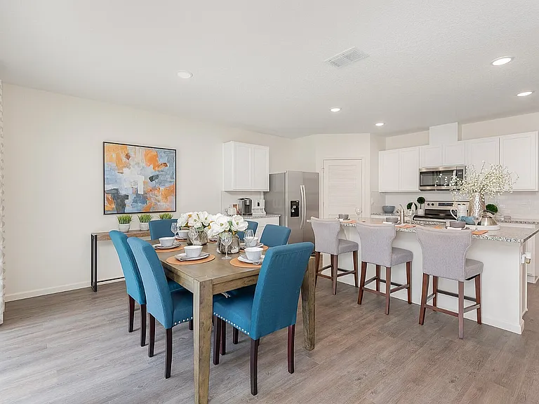 Modern dining area with vibrant blue chairs, elegant table setting, and charming decor adjacent to a sleek open-concept kitchen.