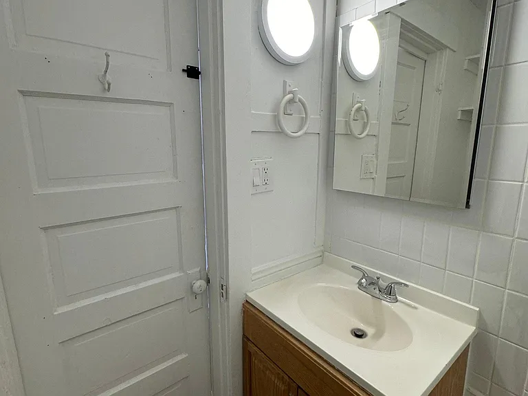 Another view of the updated bathroom featuring modern lighting, vanity storage, and classic character details.