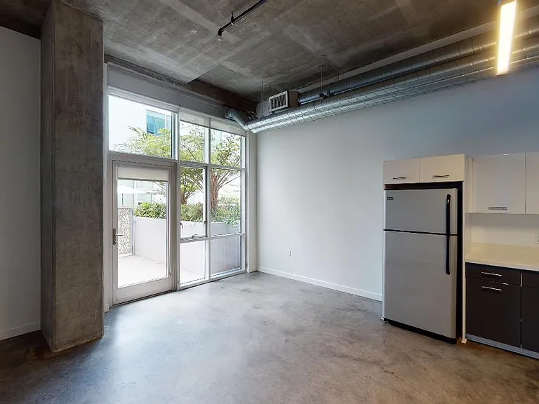 Apartment kitchen with stainless steel appliances, dining and living room with polished concrete flooring.