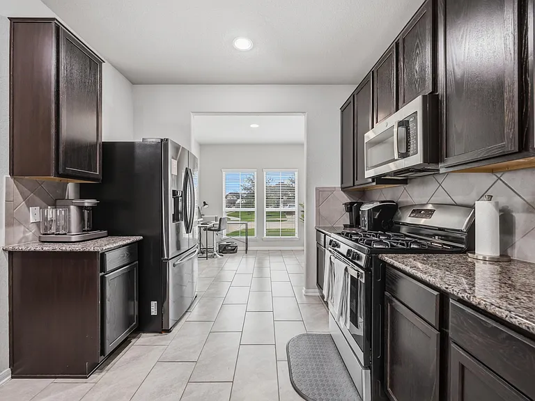 Galley kitchen with stainless steel appliances, ample cabinet storage, and tile floors, opening to a dining nook.
