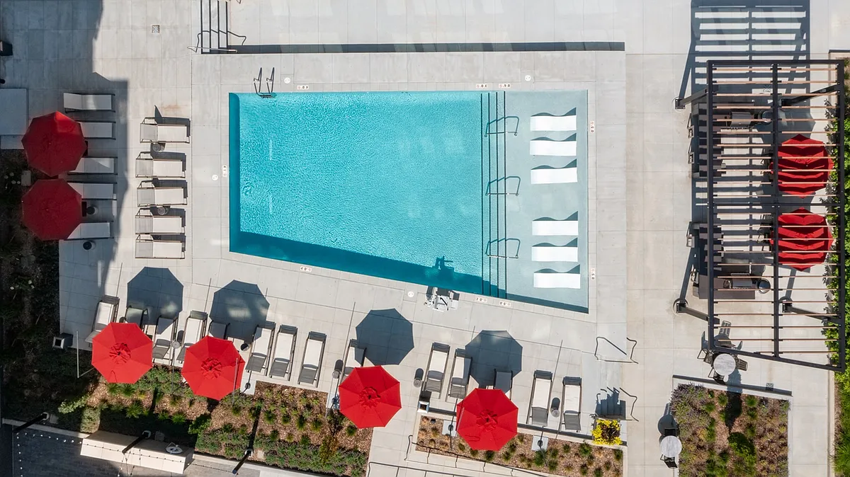 Bird's-eye view of Brickline's stunning rooftop pool deck, complete with vibrant red umbrellas and in-water loungers. - Brickline at The Mercantile