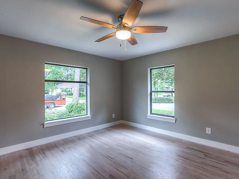 Corner bedroom in warm taupe tones with two windows, hardwood floors, and ceiling fan