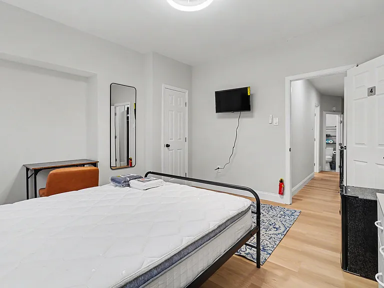 Private bedroom with a bed, desk area, full-length mirror, and wall-mounted TV, plus easy access to the hall bath.
