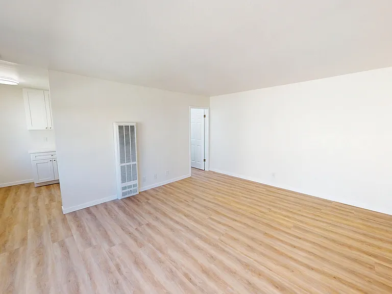 Bright and airy room with sleek wooden floors and clean white walls, leading into a cozy kitchen with modern cabinetry. Bright and airy room with sleek wooden floors and clean white walls, leading into a cozy kitchen with modern cabinetry.