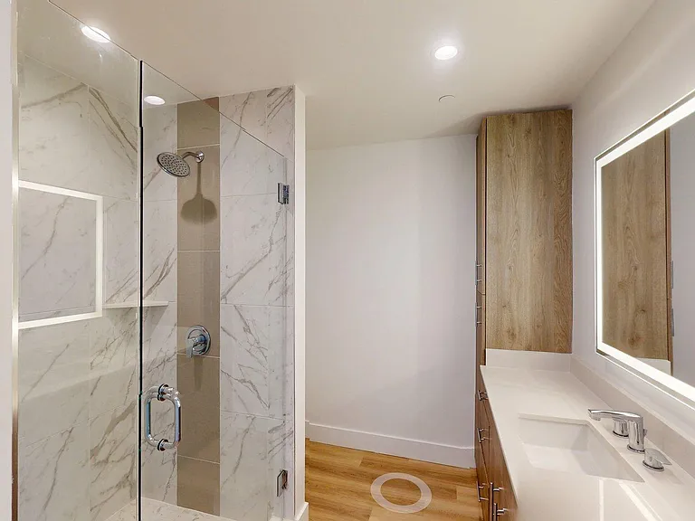 Apartment Bathroom with glass enclosed shower, LED vanity mirror and wood flooring.