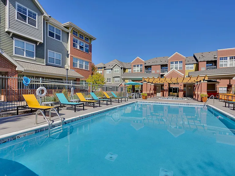 Vibrant community pool area with stylish lounge chairs, surrounded by modern townhomes under a clear blue sky.