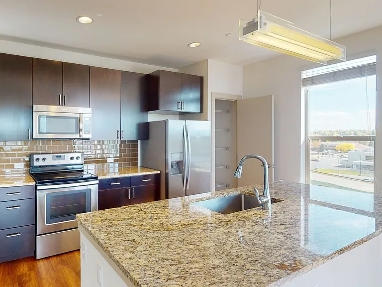 Apartment kitchen with stainless steel appliances, granite countertops and wood-style flooring.