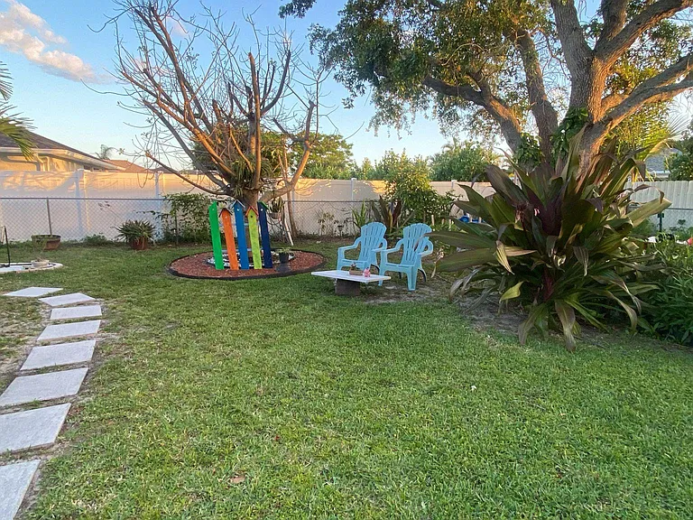 Fenced backyard with lawn, stepping-stone walkway, and a small seating areaideal for relaxing or outdoor hangouts.