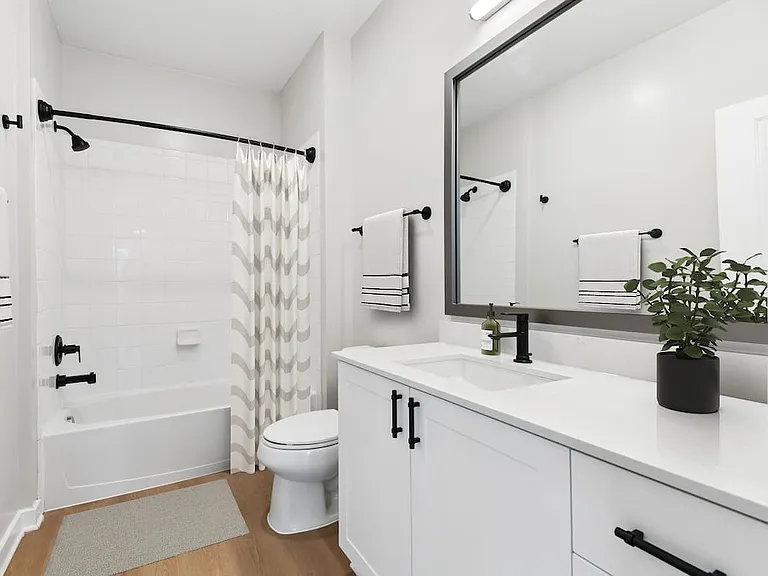 Renovated Package II bath with white quartz countertop, white cabinetry, new framed bathroom mirror, and hard surface flooring