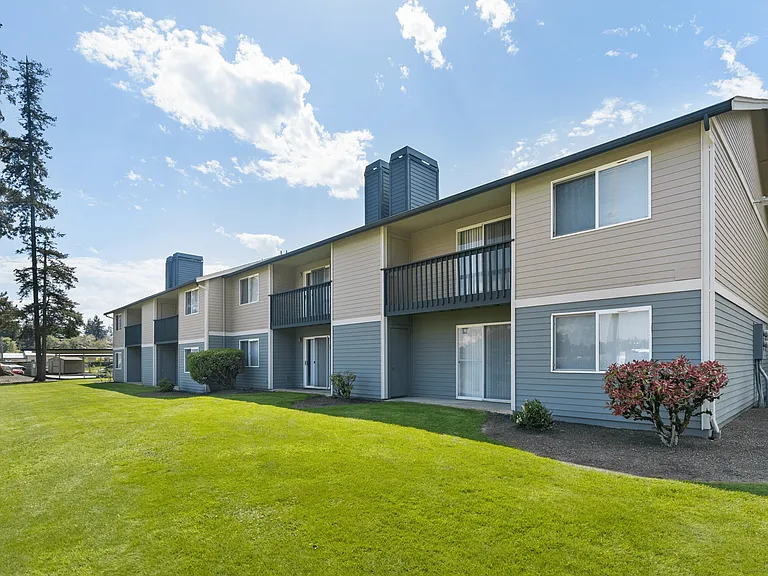Appealing apartment building with carport parking, landscaped greenery, and a clear blue sky backdrop.